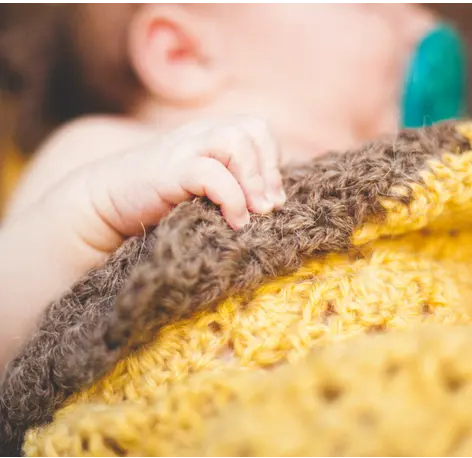 A baby’s hand holding a knitted blanket