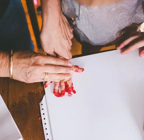 An adult helping a child make a handprint on paper